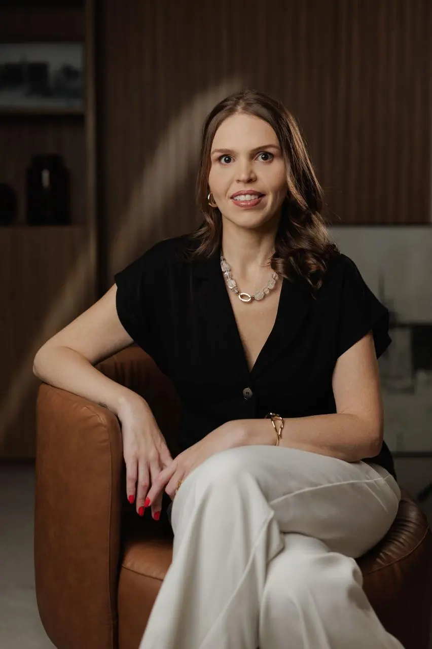 Dra. Tabata Antoniaci sentada em uma poltrona de couro, de blusa preta